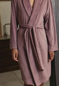 Langärmliger, mauvefarbener Bademantel aus geripptem Stoff, mit einem Gürtel in der Taille und einem Schalansatz, der eine weiche, strukturierte Oberfläche hat.