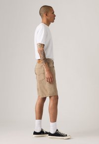 Beige denim shorts met een relaxte pasvorm, gecombineerd met een wit T-shirt met ronde hals, zwarte sneakers en witte sokken. Eenvoudige, casual stijl.