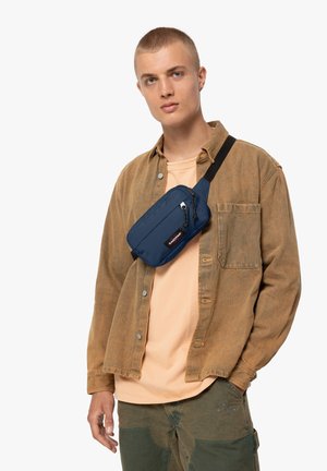 Navyblaue Bauchtasche, quer über die Schulter getragen; aus Stoff, mit Reißverschlusstasche, verstellbarem Gurt, schlanker rechteckiger Form und kleinem Logodesign.