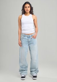 White sleeveless tank top and light blue baggy jeans. Jeans feature a faded design, with a five-pocket style and visible stitching.