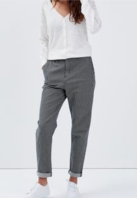 Vitt knäppbart cardigan med spetsdetaljer på ärmarna, parat med svartvita randiga byxor, uppvikta fållar, och vita sneakers.