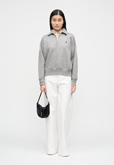 Sivi pulover z zadrgo na ovratniku, bele široke hlače in majhna črna torbica. Preprost dizajn, gladka tekstura in nevtralna barvna paleta.