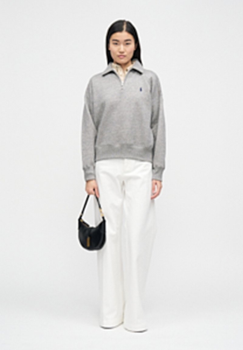 Pull gris avec col à fermeture éclair, pantalon blanc à jambes larges, et petit sac à main noir. Design simple, texture lisse et palette de couleurs neutres.