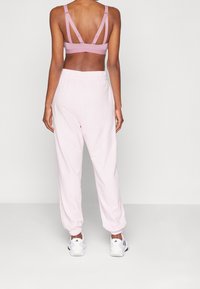 Idrottsbehå i mjuk rosa med korsade remmar, i kombination med ljusrosa joggers med elastisk midja och smalnade anklar.