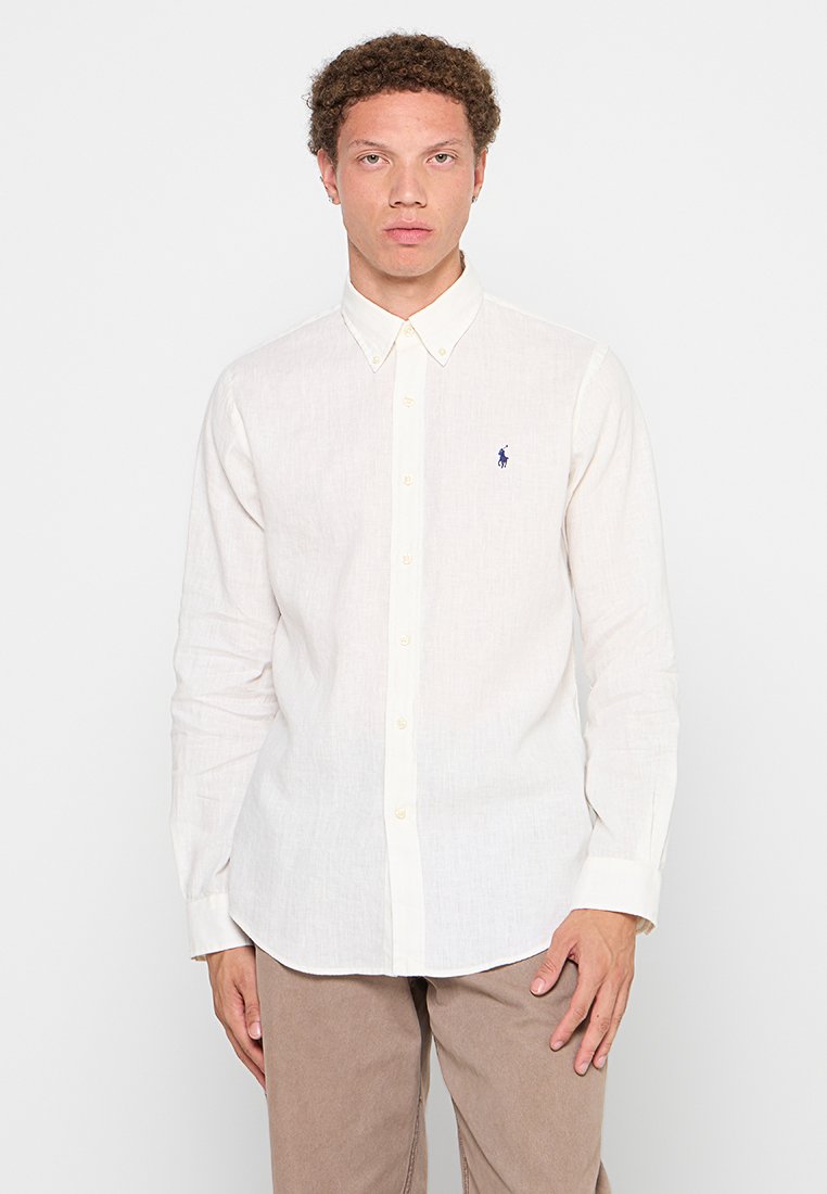 Chemise blanche à manches longues en lin, dotée d'un col étalé et d'un petit logo bleu brodé sur la poitrine.
