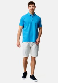 Lyseblå polo skjorte med krage, hvite shorts med oppbrett og svarte joggesko. Enkelt, glatt stoff med en subtil logo på brystet.