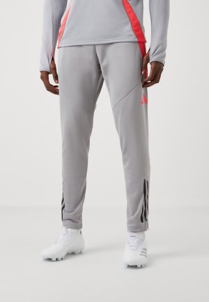 Graue Sporthosen mit pinken Akzenten, taillierter Passform und schwarzem Streifenmuster an den Säumen. Getragen mit weißen Fußballschuhen.