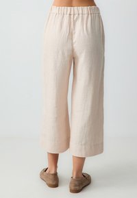 Lichtroze linnen culottes met een elastische tailleband, een cropped wijde pijp en een textuurafwerking. Gepaard met zachte, neutraalgekleurde schoeisel.