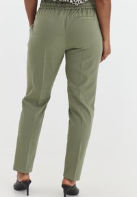 Pantalons fuselés vert olive avec une taille élastique, poches avant et une poche arrière simple. Texture lisse avec une coupe ajustée.