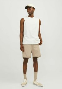 Chemise sans manches blanche, short beige, chaussettes beiges et baskets beiges. Une casquette de couleur claire avec un logo complète la tenue.