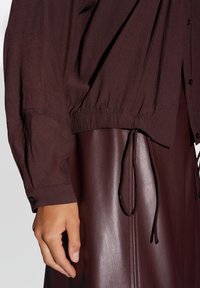 Bordeaux geklede blouse met elastische manchetten en een geraffineerde zoom, gecombineerd met een bijpassende bordeaux leren rok met een strikdetail.