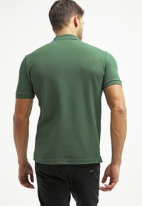 Groene polo met korte mouwen gemaakt van textuurstof, met een kraag en een rechte zoom. De achterkant toont een gladde contour met aansluitende mouwen.