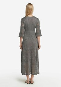 Lång grå stickad klänning med ribbad textur och trekvarts bjällersärmar. Har intrikata spetsmönster vid fållen och midjan.