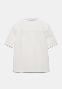 Biała koszula z krótkim rękawem, ze prostym karczkiem na plecach i luźnym krojem, przedstawiona na jednolitym jasnoszarym tle.