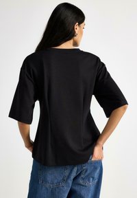 Maglietta nera oversize con scollatura rotonda e maniche corte, realizzata in materiale morbido. Presenta una vestibilità rilassata e spacchi laterali.