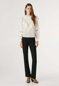 Vit blus med volangkrage och ärmar, med spetsdetaljer och genomskinliga inslag, tillsammans med svarta tajta jeans och taupefärgade klackar.