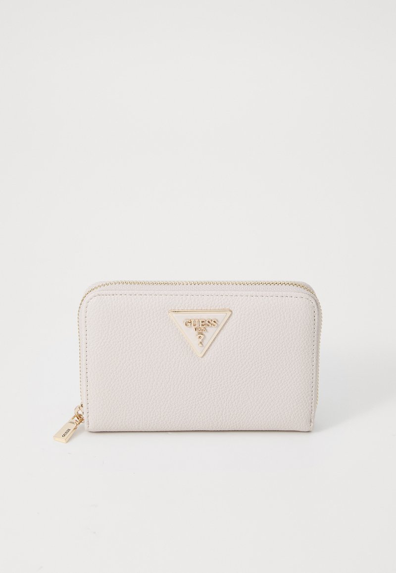 Beige strukturiertes Portemonnaie mit einer goldenen Guess-Logo-Plakette, Reißverschlussverschluss und einem kleinen Anhänger, das eine glatte und polierte Oberfläche aufweist.