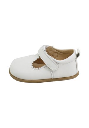 Zapato de cuero blanco con puntera redondeada, que presenta un diseño de corte escallopado, una correa de Velcro y una suela de goma color marrón.