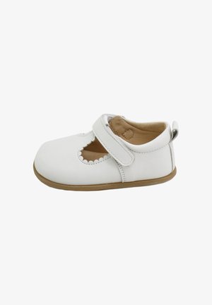 Zapato de cuero blanco con puntera redondeada, que presenta un diseño de corte escallopado, una correa de Velcro y una suela de goma color marrón.