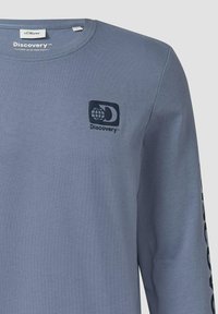 Grijze longsleeve t-shirt van katoen, met een zwart logo op de borst en tekst gedrukt langs de mouw. Gladde textuur.