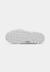 Weiße Sneakersohle aus strukturiertem Gummi, mit dreieckigen Grippatterns und einer glatten Mittelfläche. Abnutzungsspuren sind sichtbar.