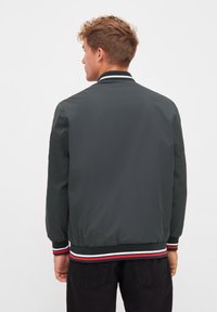 Grå bomberjacka med ribbat krage och ärmslut som har röda, vita och marinblå ränder. Slät, lätt material och avslappnad design.