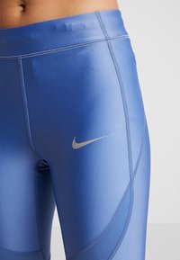 Legginsy sportowe z wysokim stanem w gradientowym niebieskim kolorze, z logo Nike w kolorze srebrnym oraz kontrastowymi szwami.