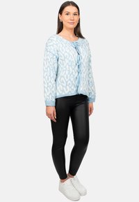 Cardigan leopard print azzurro con fronte a fiocco, morbido in maglia, maniche lunghe, abbinato a leggings neri lucidi e sneaker bianche.