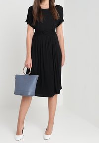 Mustat polvenpituinen mekko lyhyillä hihoilla, kerrostettu vyötärön yksityiskohta, yhdistetty vaaleansiniseen käsilaukkuun, jossa on hopeiset yksityiskohdat ja jämäkkä muoto.