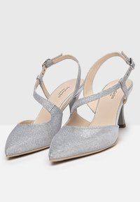 Escarpins argentés à bride arrière avec un bout pointu, une légère brillance, un design à lanières croisées et un talon moyen bloc. Doublure intérieure lisse.
