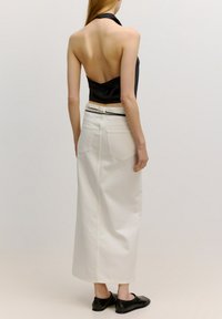 Zwarte haltertop met open rug, gecombineerd met een lange witte denimrok. Zwarte platte schoenen maken de outfit compleet.