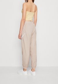 Beige lightweight joggers with elastic cuffs and pockets, paired with a fitted yellow strapless top. White sneakers complete the look.