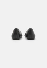 Ballerines noires en cuir avec un bout rond, texture lisse, détails minimalistes, et un petit nœud sur le côté, dotées d'un petit talon.