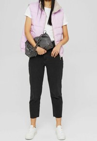 Chaleco de plumas púrpura claro con un cuello beige, camiseta blanca, jeans cortos negros y zapatillas blancas; lleva una bolsa gris con un asa de cadena.