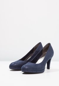 Zapatos de tacón alto azul marino con un upper de tela texturizada y acentos brillantes en la punta, que presentan una punta redondeada y un diseño de tacón delgado.