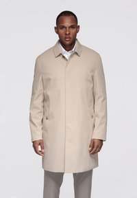 Abrigo beige hasta la rodilla con corte recto, cuello alargado y bolsillos laterales. Presenta herrajes en tono dorado en los bolsillos y una textura suave.