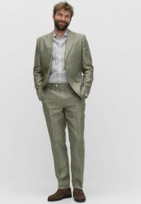 Ljusgrön linnekostym med slim fit, kombinerad med en vit och blårandig skjorta. Bruna läderskor fulländar outfiten.