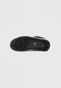 Μαύρη και μπεζ σόλα αθλητικού παπουτσιού με υφασμάτινα μοτίβα και χρυσό λογότυπο Jumpman στο κέντρο της σόλας σε λευκό φόντο.