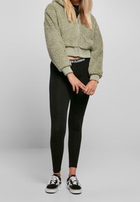 Grön fleecekortad hoodie med texturerad tyg, tillsammans med svarta leggings med en märkesskärp. Svarta låg-top sneakers avslutar looken.