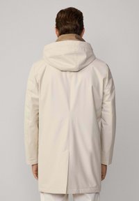 Abrigo impermeable beige claro con capucha, con un contraste en la parte interna del cuello en marrón. Diseño sencillo con mangas largas y corte recto.
