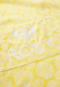 Asciugamano giallo con motivo di margherite bianche; presenta un logo ricamato bianco "ROXY" e un design a cuore. Texture morbida, forma rettangolare.