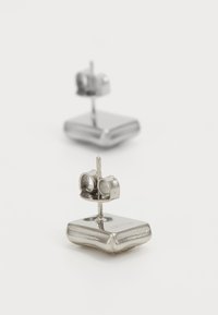 Sølv studs med firkantet base og afrundede kanter. Har en stift med en lille, cirkulær detalje foroven. Poleret finish.