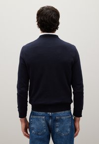 Maglione leggero blu navy con collo e polsini a coste, abbinato a jeans in denim blu sbiadito con tasche posteriori.