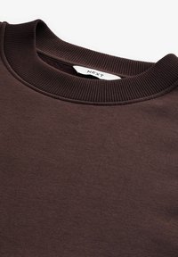 Sudadera marrón con cuello acanalado, tejido texturizado y un sutil patrón jaspeado. La etiqueta dice "NEXT".