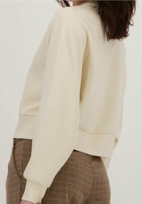 Sudadera color crema con mangas largas y estrechas, puño acanalado y un ajuste relajado. Tejido texturizado con una superficie suave.