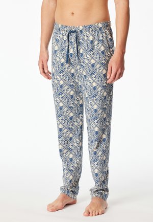 Man wearing blue and beige patterned drawstring pajama pants, standing barefoot against a white background.