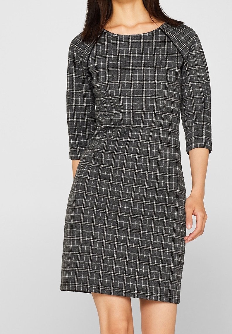 Musta ruudullinen mekko, jossa on tiukka muotoilu, kolme neljännestä hihaa ja pyöreä pääntie. Valmistettu teksturoidusta kankaasta, jossa on valkoisia yksityiskohtia.