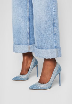 Gekrempelte hellblaue Jeans, getragen mit spitzen blauen Stilettos, verziert mit kleinen Strasssteinen.