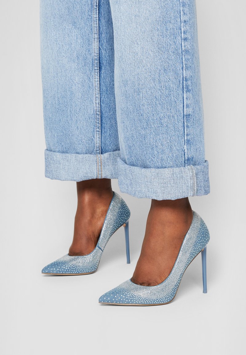 Jean bleu clair retroussé, porté avec des talons aiguilles pointus bleus ornés de petits strass.