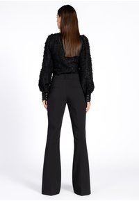 Zwarte, textuur gevende top met lange mouwen en pofmouwen, gecombineerd met hoge zwarte flared broek met knoopdetails op de manchetten.